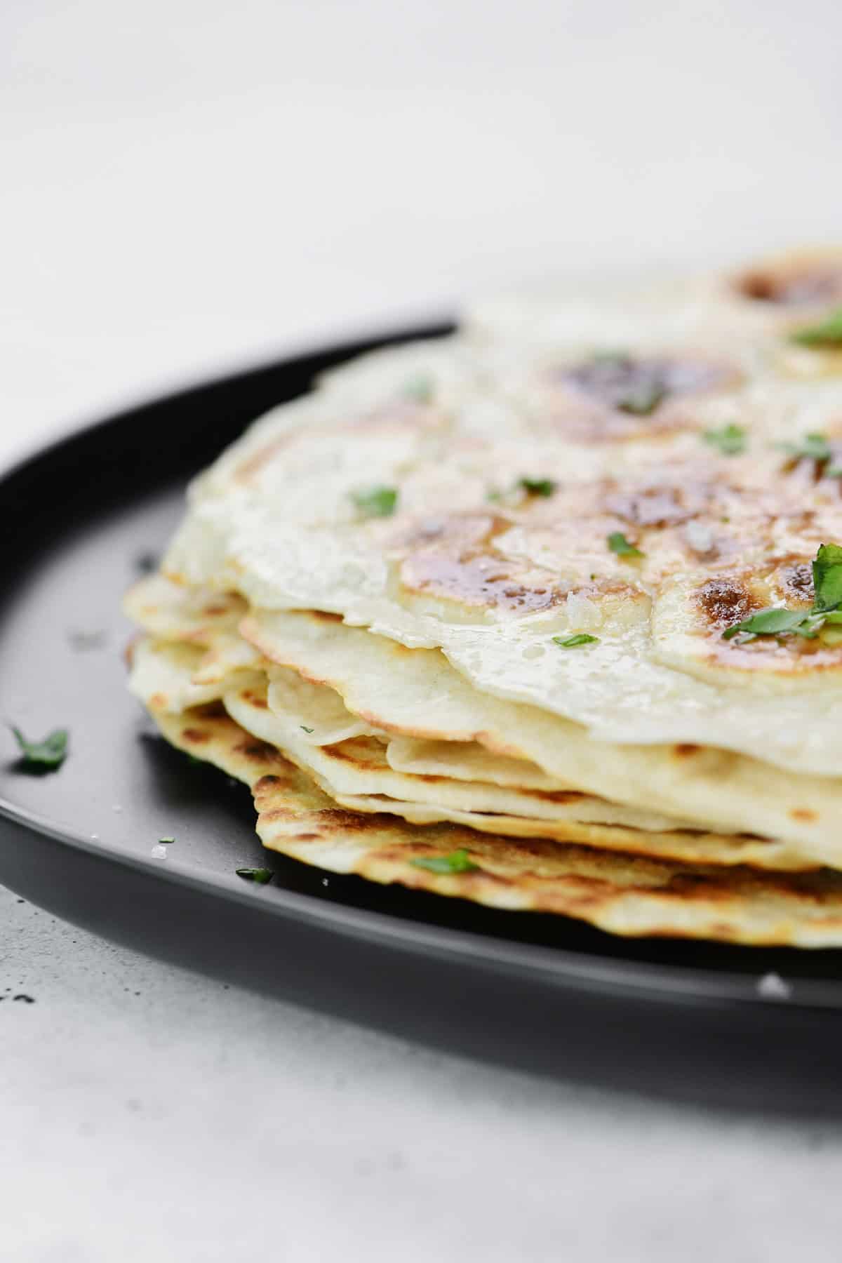 A stack of six cottage cheese flatbread on a black plate.