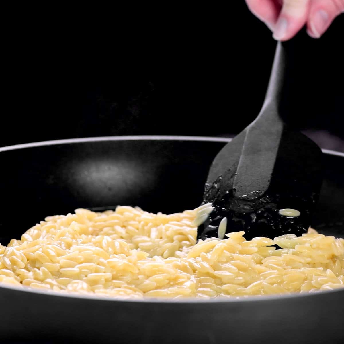 Stirring lemon orzo in a skillet.