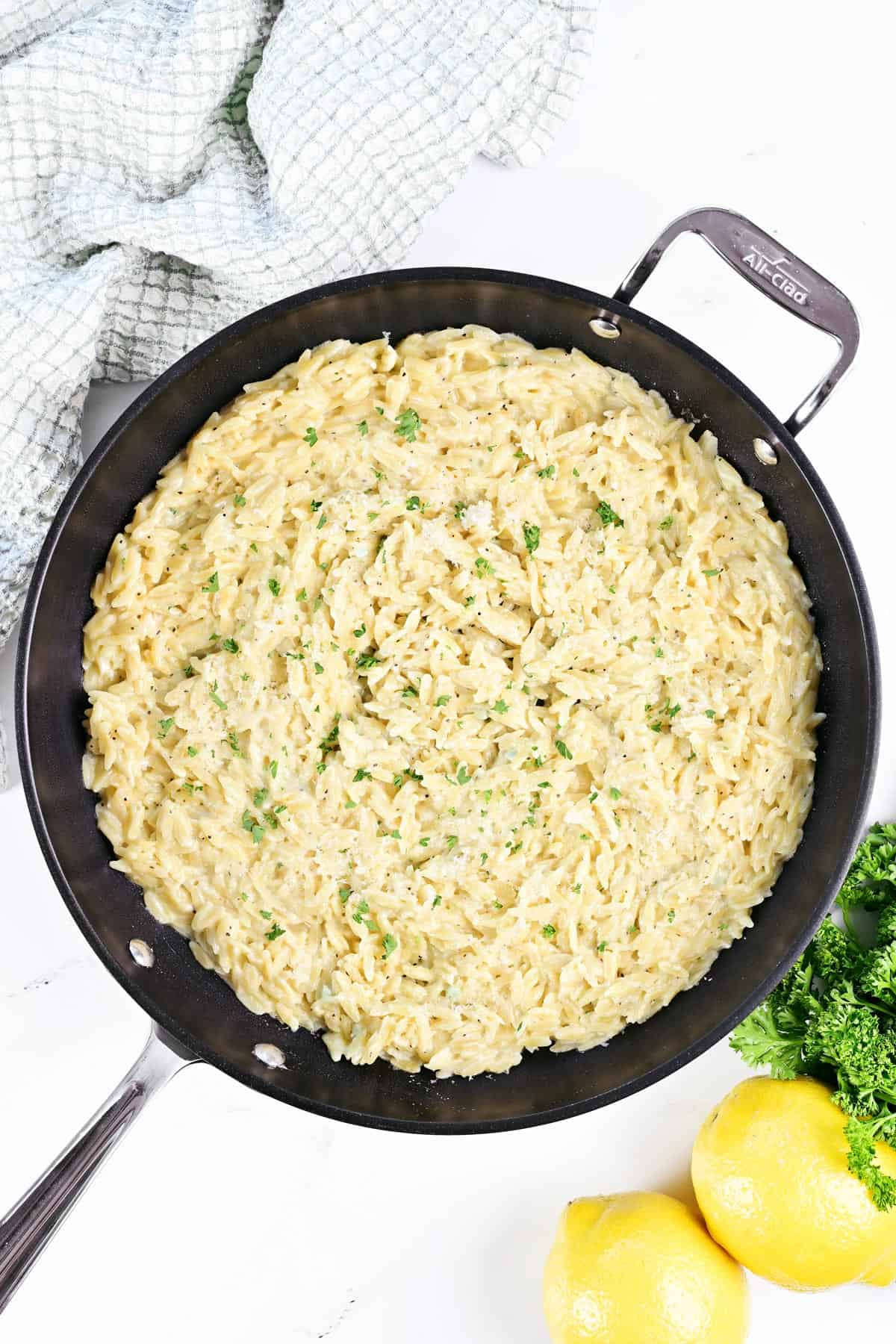 Creamy lemon orzo in a skillet with parsley and lemons.