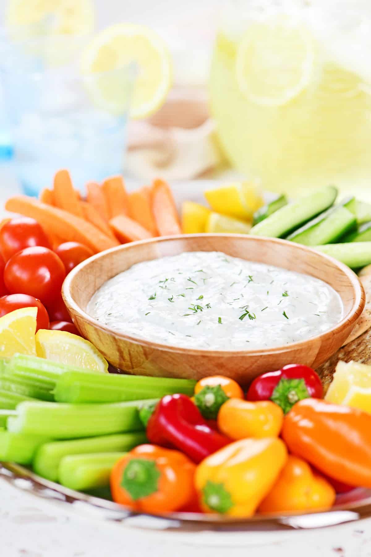 Cucumber dill sauce in a wooden bowl surrounded by veggies, fruit, and crackers.