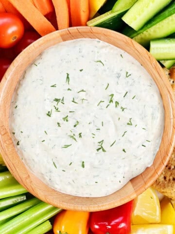 Cucumber dill sauce in a wooden bowl surrounded by veggies, fruit, and crackers.