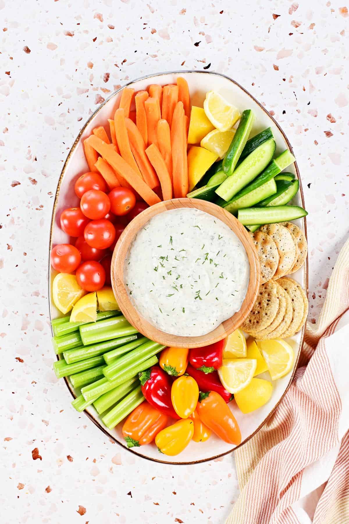 Cucumber dill sauce in a wooden bowl surrounded by veggies, fruit, and crackers.