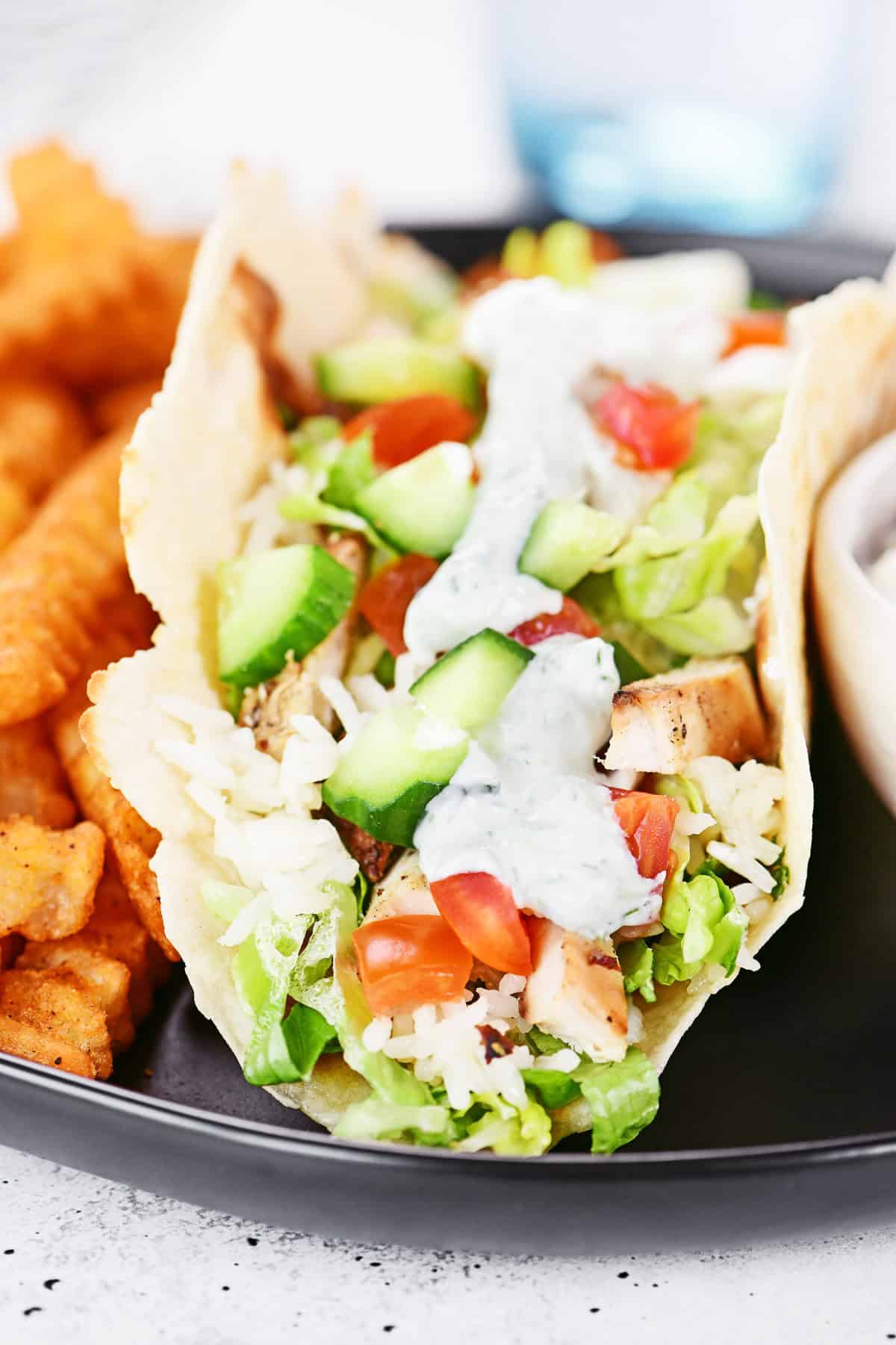 Greek chicken wrap on a plate with seasoned fries.