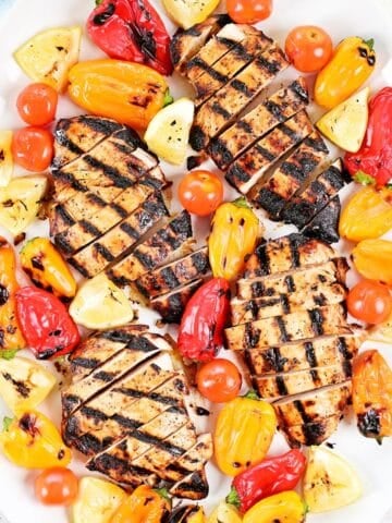 Greek chicken marinade on grilled, sliced chicken on a platter with peppers, tomatoes, and lemons.