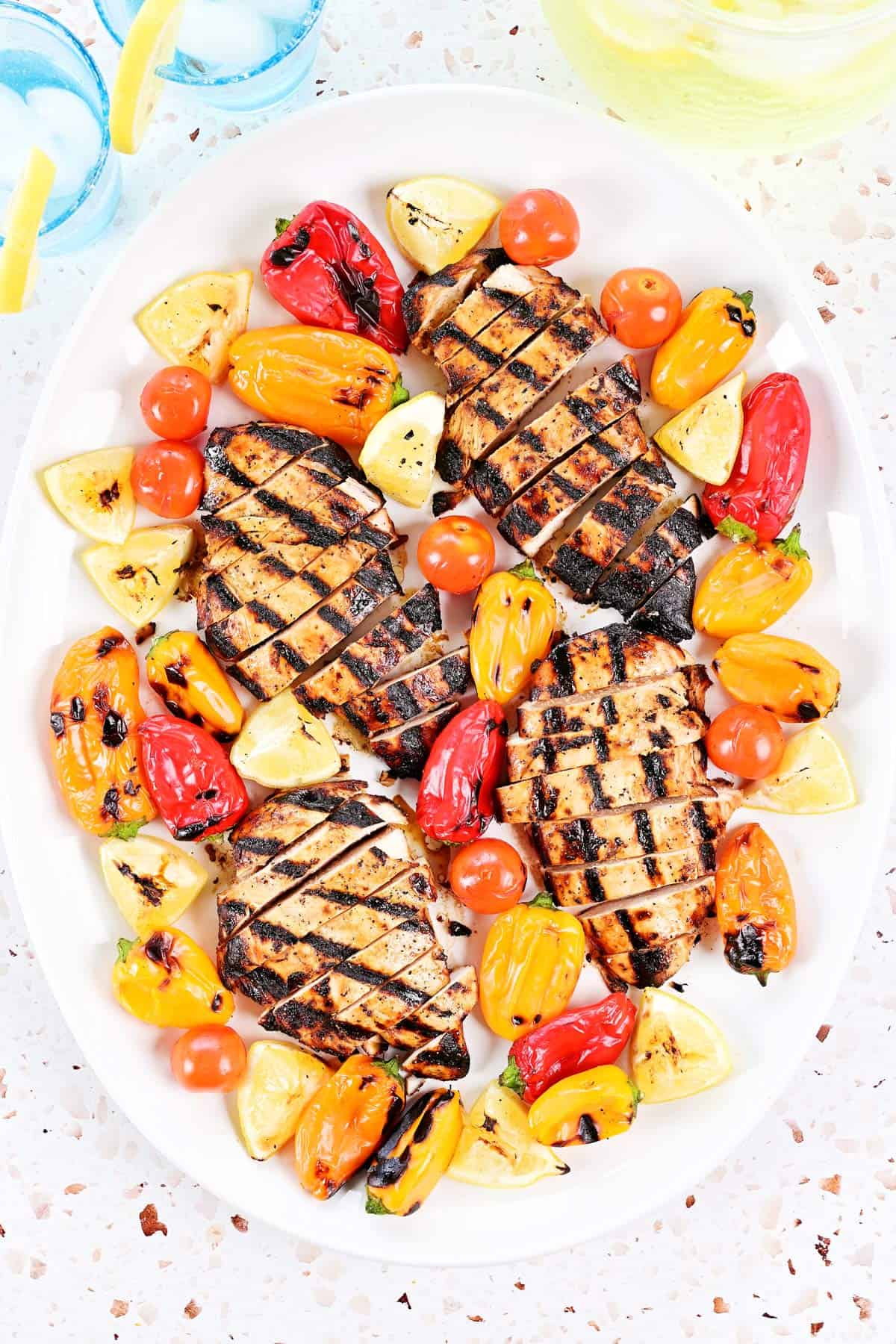 Greek chicken marinade on grilled, sliced chicken on a platter with peppers, tomatoes, and lemons.