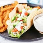 Greek chicken wrap on a black plate with fries and dip.