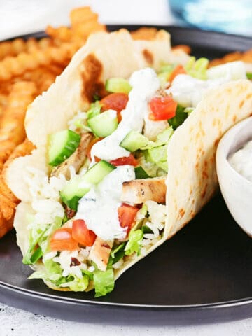 Greek chicken wrap on a black plate with fries and dip.