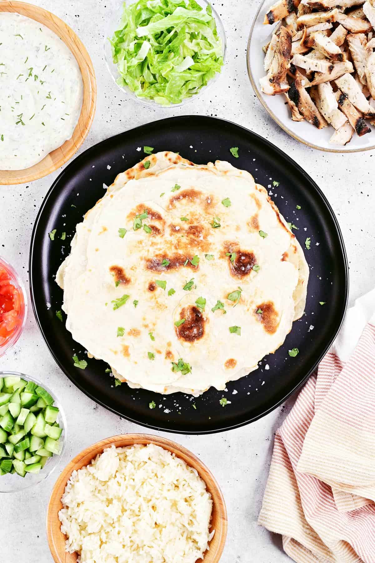 Greek chicken wrap ingredients on plates and in bowls.