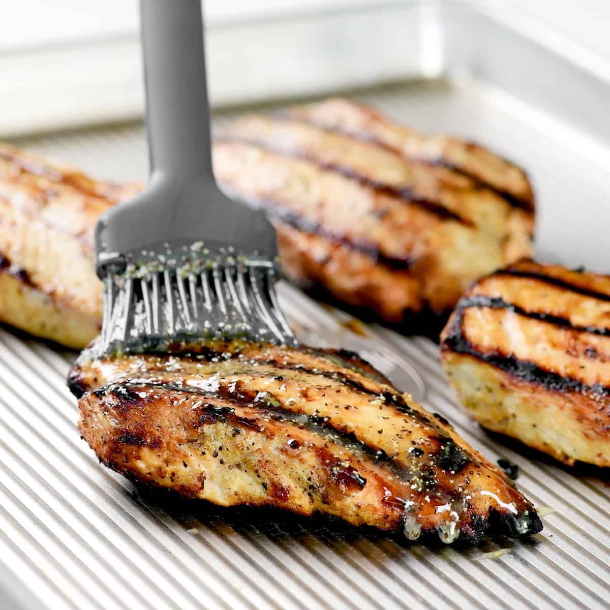 Brushing seasoned melted butter over grilled chicken breasts.