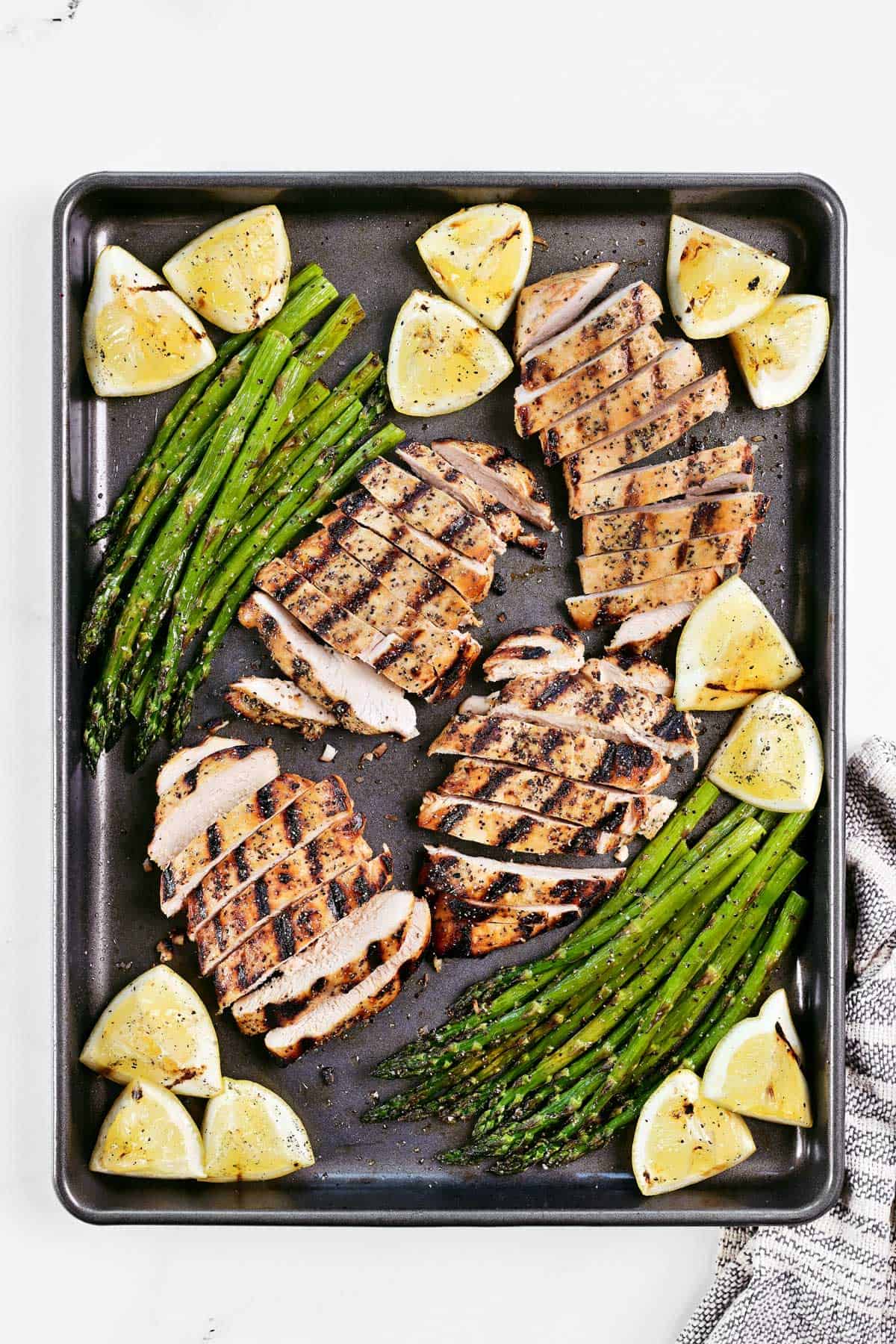 Lemon pepper chicken marinade grilled chicken, asparagus, and lemon wedges on a baking sheet.