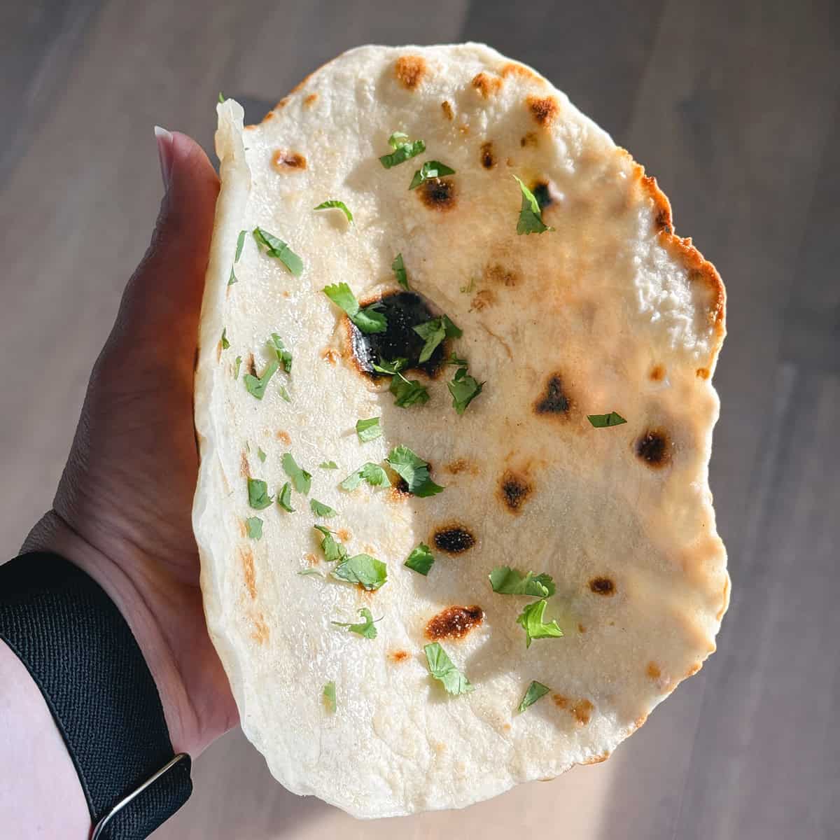 A hand holding a piece of cottage cheese flatbread.