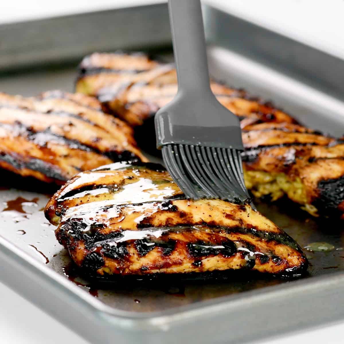 Brushing melted butter on grilled chicken breasts.