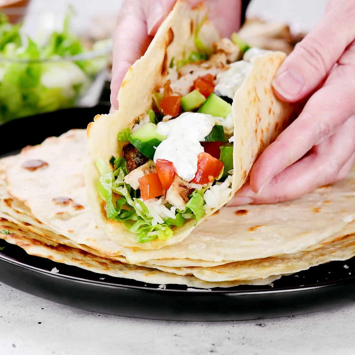Hands folding a Greek chicken wrap.