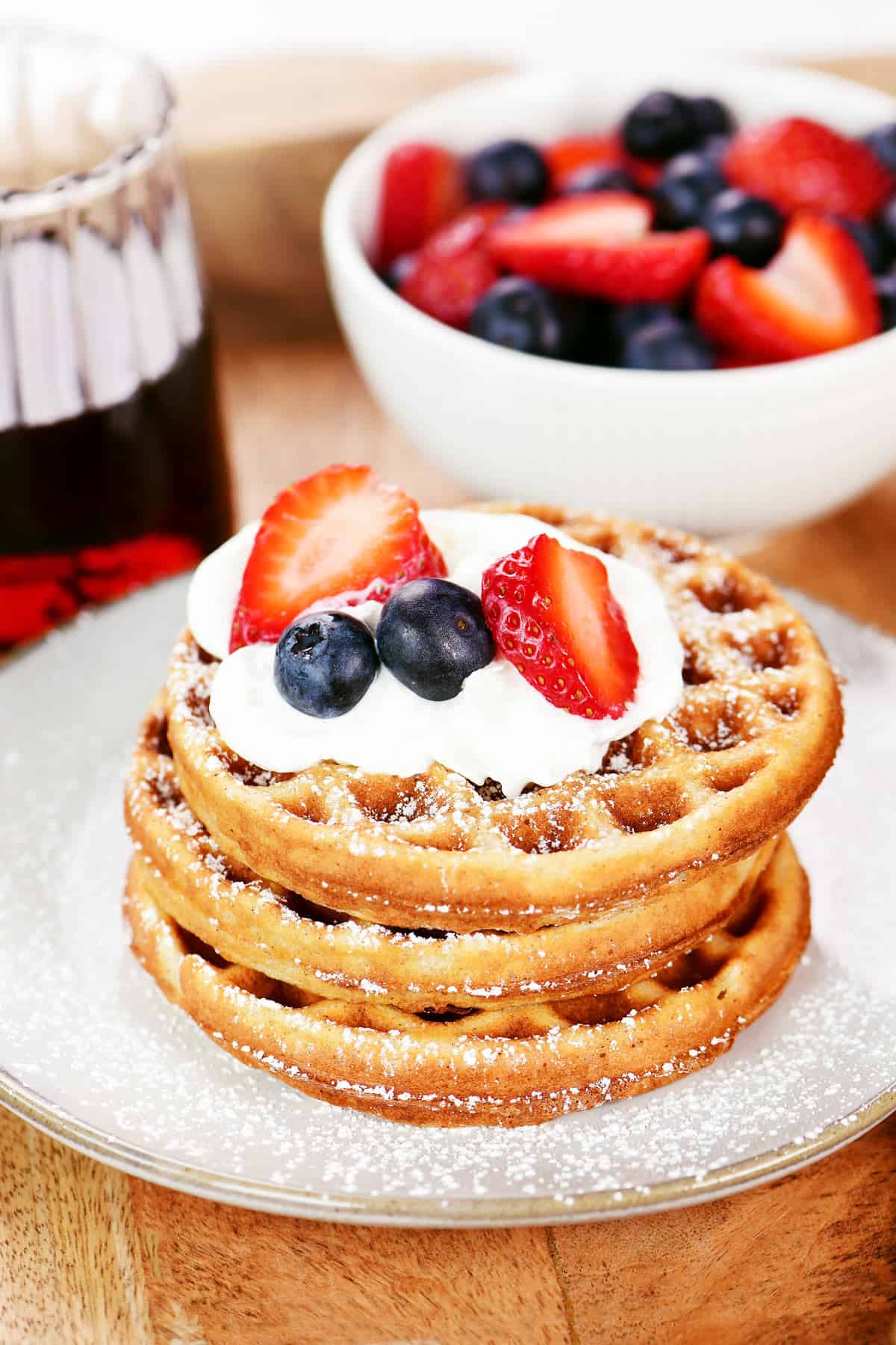 Three cottage cheese protein waffles on a plate with powdered sugar, whipped cream, and berries on top.