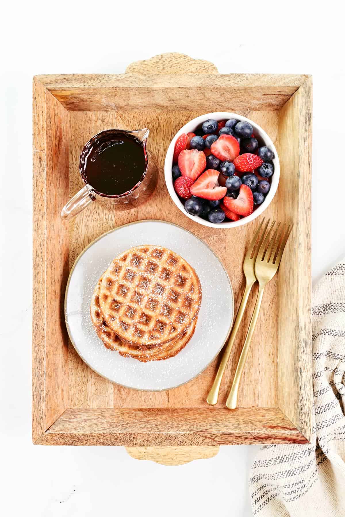 Three cottage cheese waffles plated on a wooden tray with fruit and maple syrup.