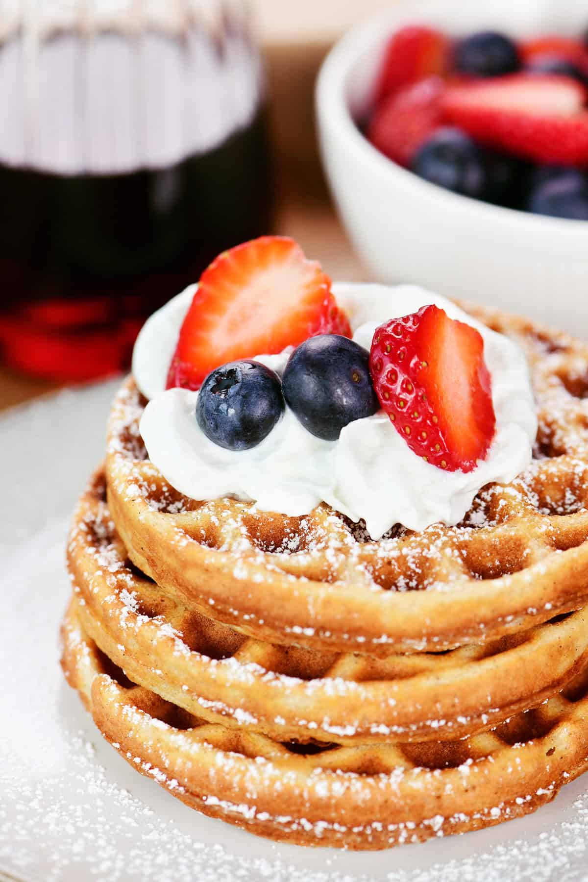 A stack of cottage cheese waffles with whipped cream and fruit.