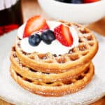 Three cottage cheese waffles with whipped cream, strawberries, and blueberries on top.
