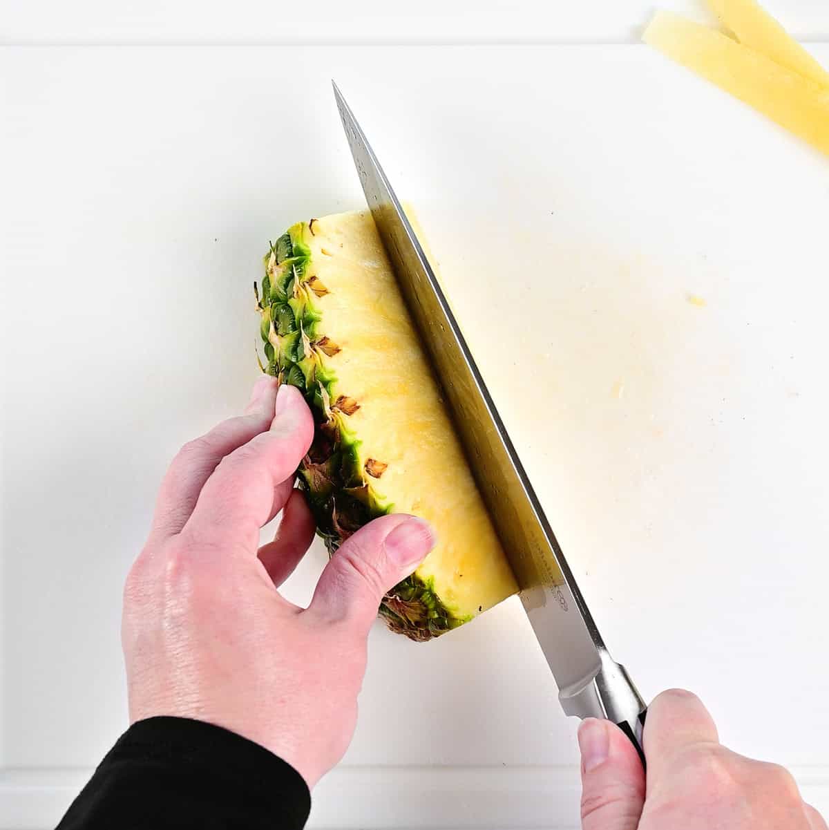 Cutting a pineapple spear on a white cutting board.