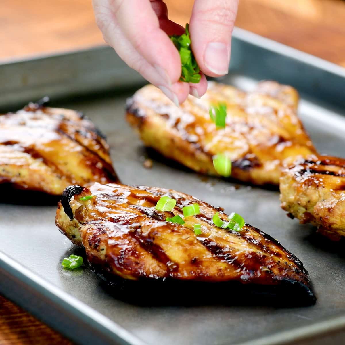 Sprinkling sliced green onions on a chicken breast.