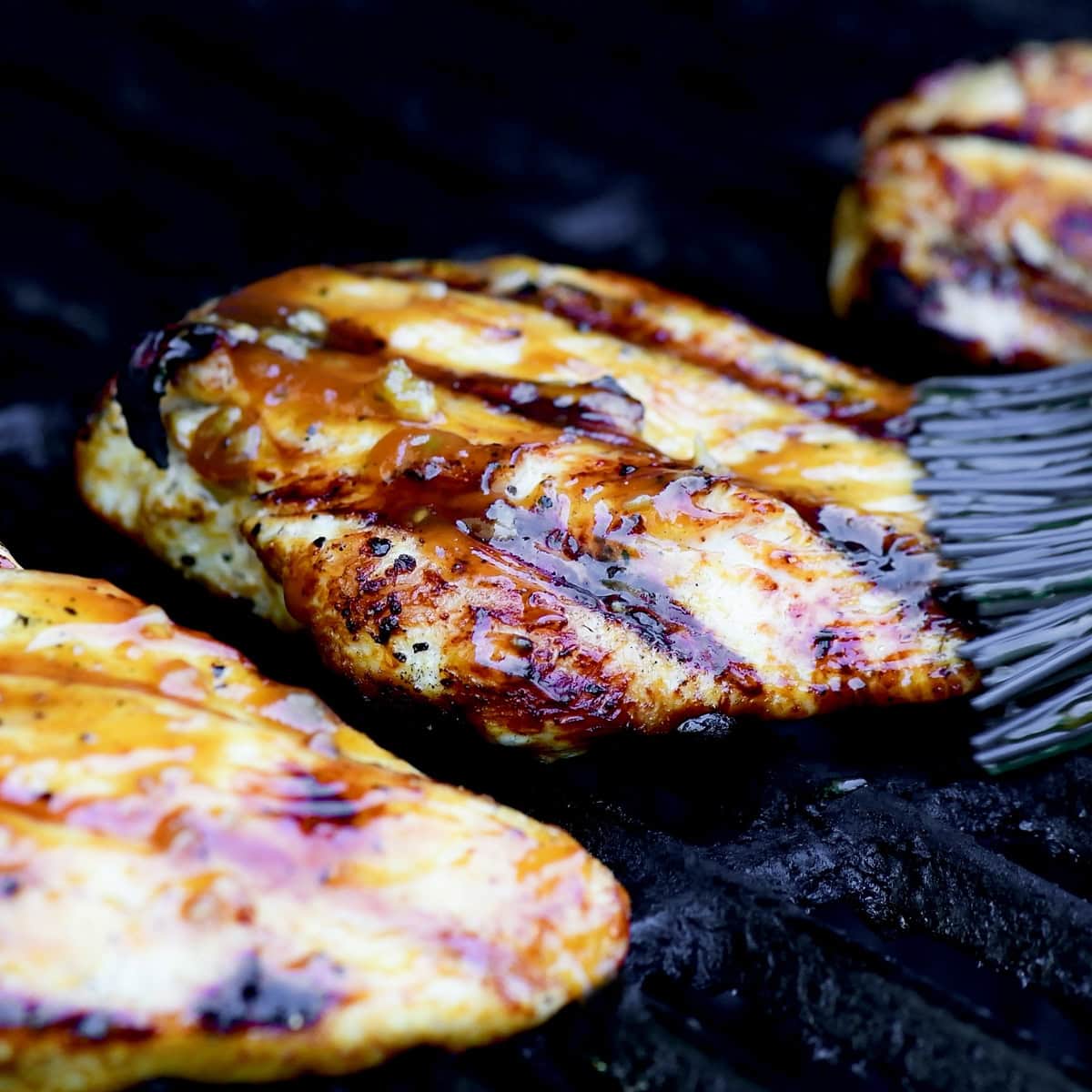 Brushing sauce on a chicken breast on the grill.