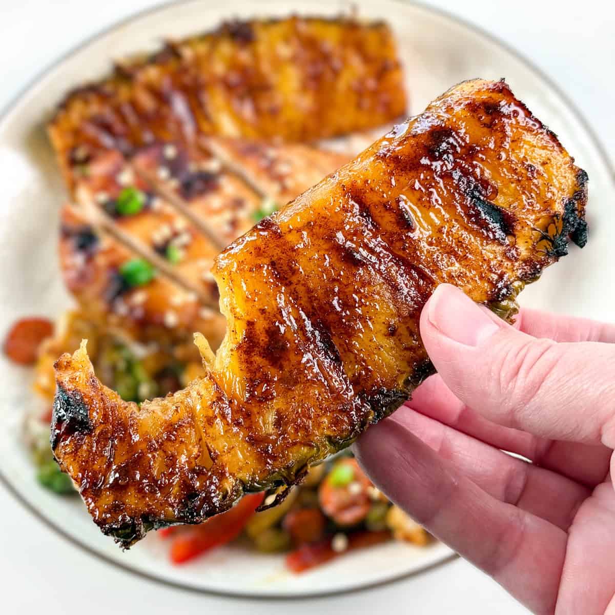 A hand holding a piece of grilled pineapple with a bite taken out of it.