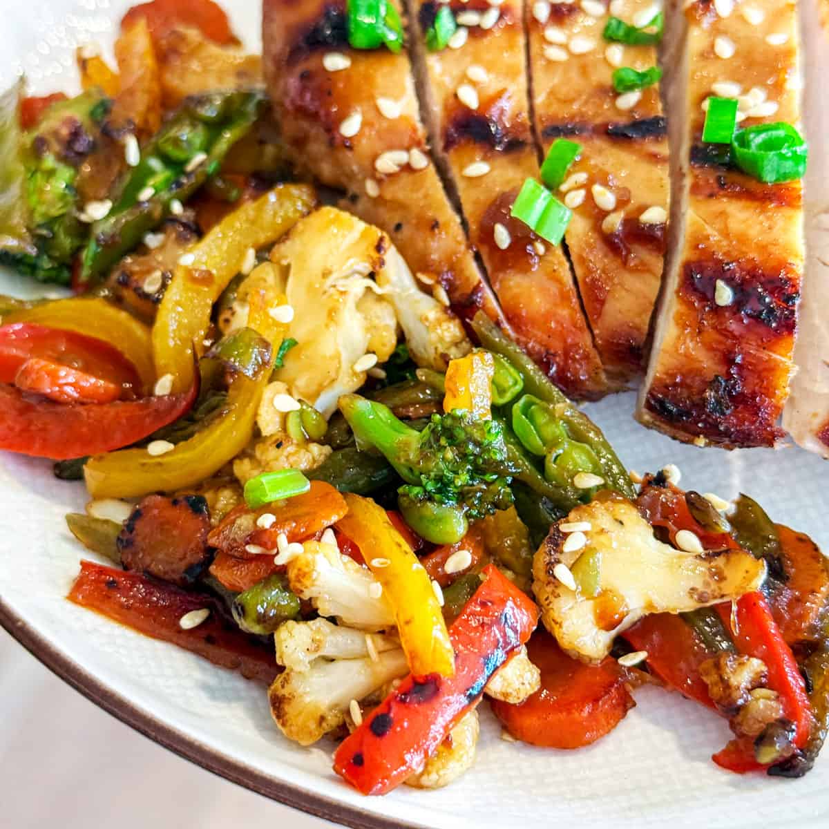 Stir vegetables on a white plate with teriyaki chicken.