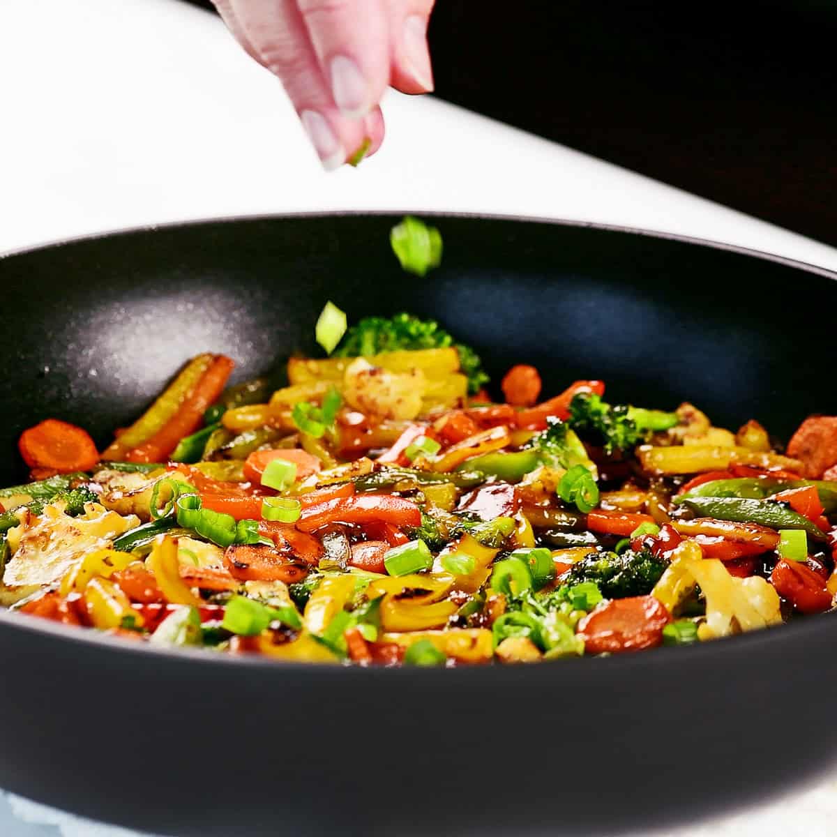 Sprinkling sliced green onions in pan.