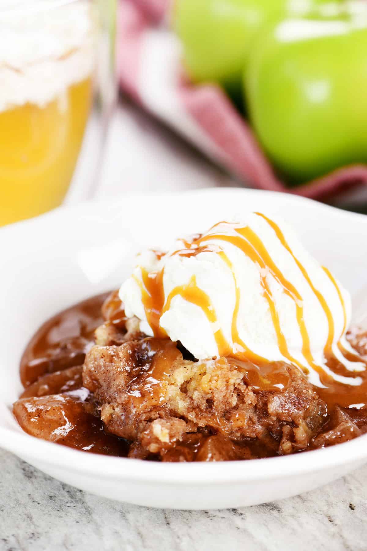 Slow cooker apple dump cake in a white bowl with ice cream on top.