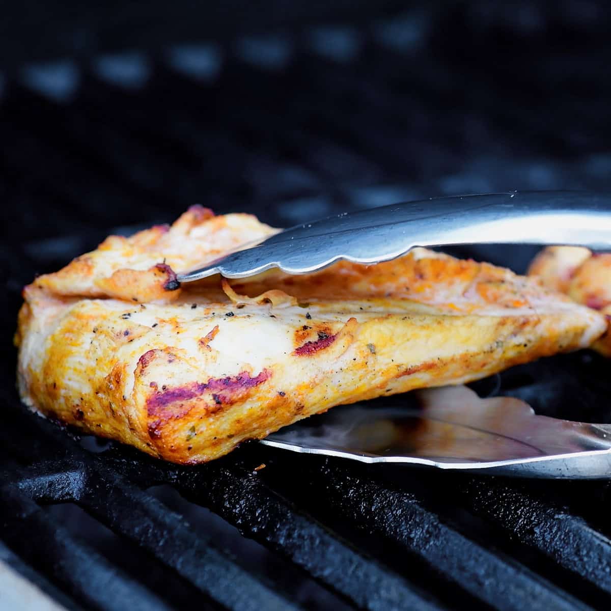Using tongs to lift buffalo chicken breast from the grill.