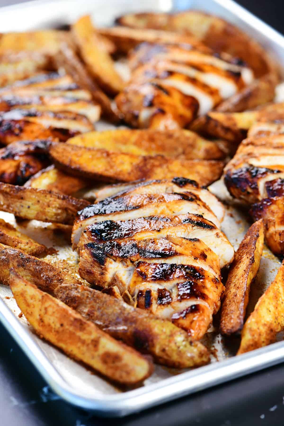 Buffalo chicken marinade grilled chicken on a sheet pan with potato wedges.